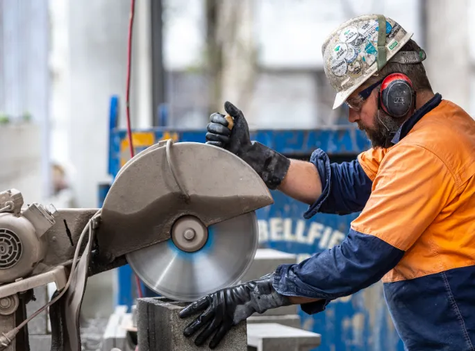 Worker wearing PPE while using a buzz saw on a piece of metal