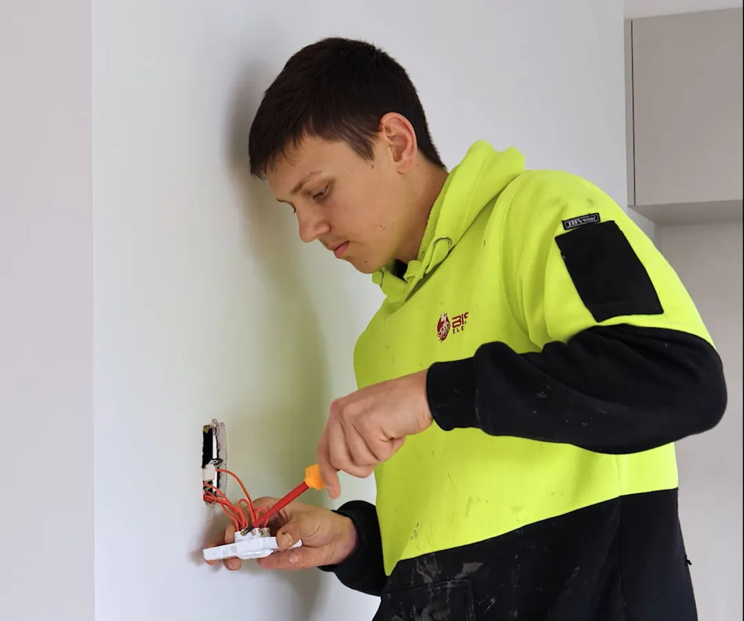Worker wearing hi vis working on electric socket in a wall