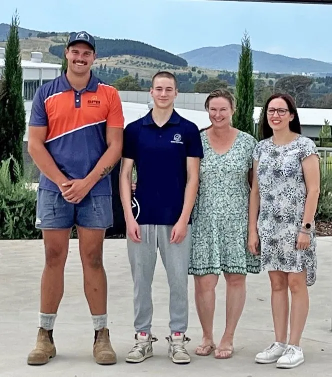 Four people standing together outdoors with a scenic background behind them