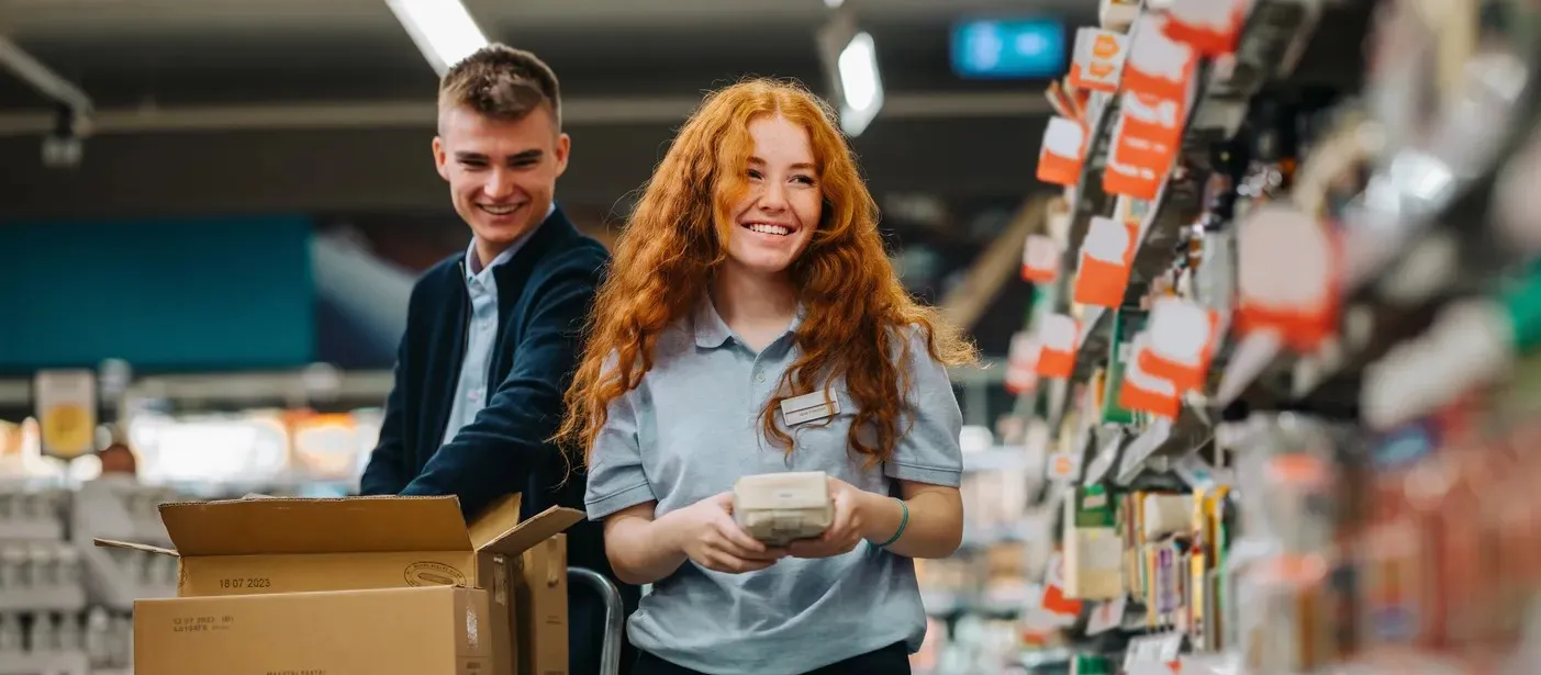 Two workers wearing uniforms unpacking groceries at a grocery store