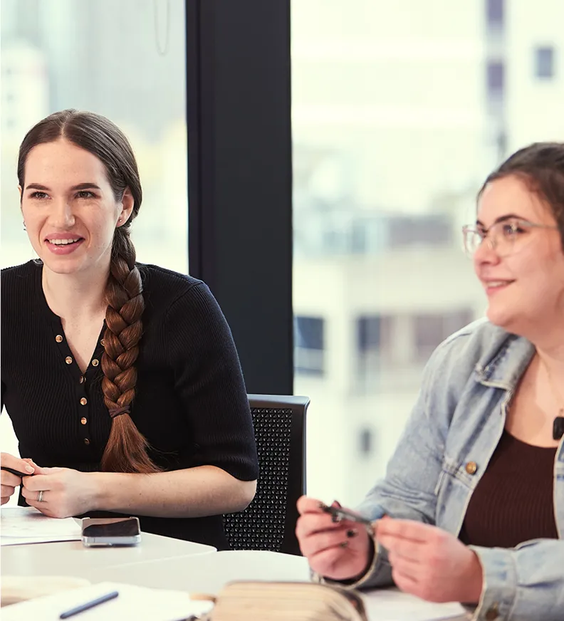 Two people in an office setting at a table participating in a discussion